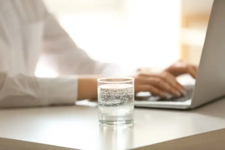 Kullsyrevann i et glass på en kontorpult ved siden av person som jobber på pc-en
