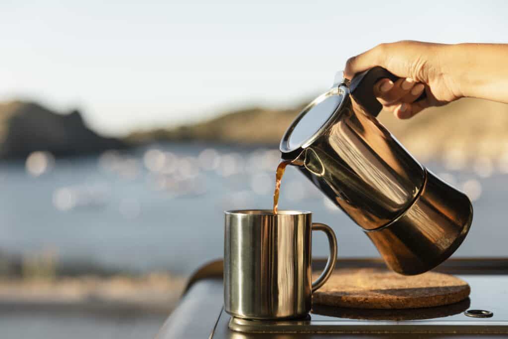 Kaffe som helles fra en kaffekanne i en kopp omgitt av fin natur.