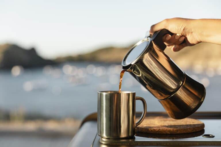 Kaffe som helles fra en kaffekanne i en kopp omgitt av fin natur.