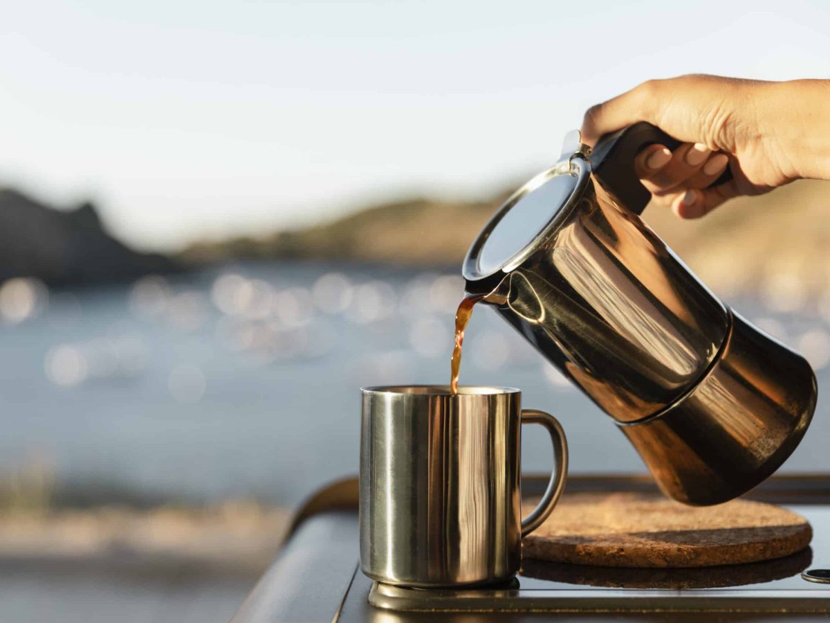 Kaffe som helles fra en kaffekanne i en kopp omgitt av fin natur.