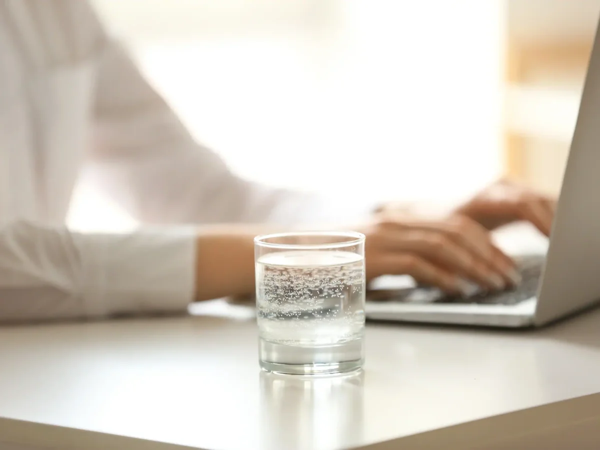 Kullsyrevann i et glass på en kontorpult ved siden av person som jobber på pc-en